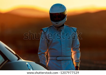 A Helmet Wearing Race Car Driver In The Early Morning Sun Looking At His Car Before Starting