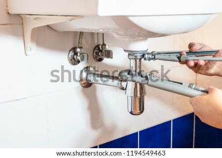 plumber fixes sink siphon by two pipe-wrenches in bathroom