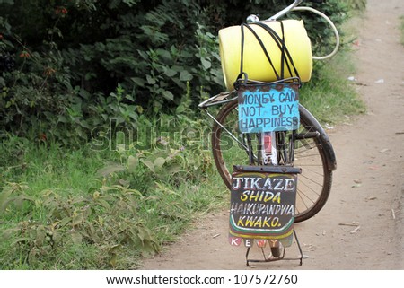 A bicycle carrying an important message (Money Can Not Buy Happiness) in Kenya, Africa. The yellow container is for freshwater.