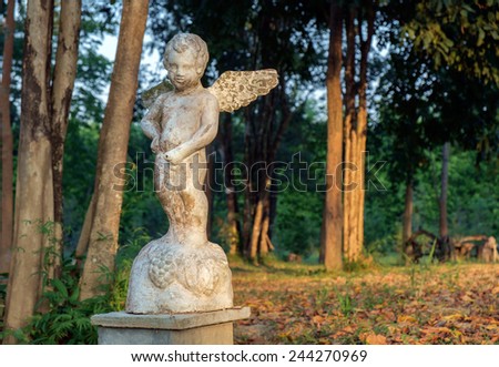 Old and dirty statue of cupid standing in the garden.
