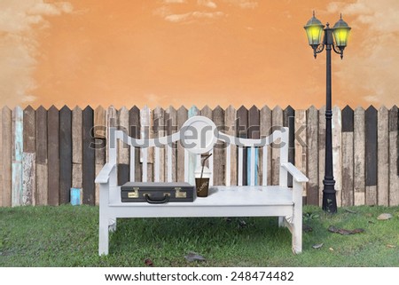 White bench with business suitcase on lawn. on evening sky background. Digital retouch.
