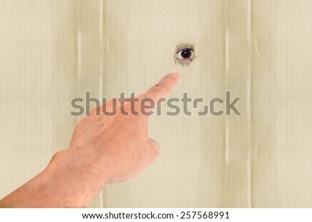 Human hand pointing on eye looking through hole.