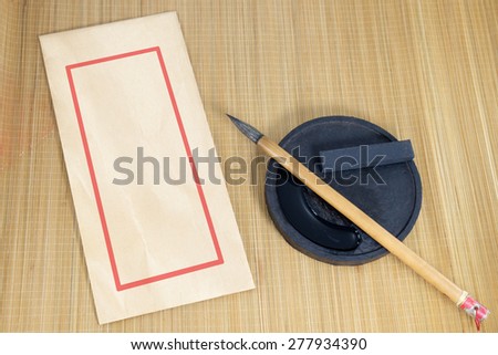 Chinese writing brush and ink for calligraphy and envelope placed on bamboo background.