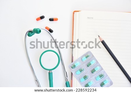 Blank writing book with pencil ,pills and stethoscope on white table.