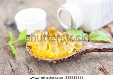 Cod liver oil omega 3 gel capsules on wooden spoon.