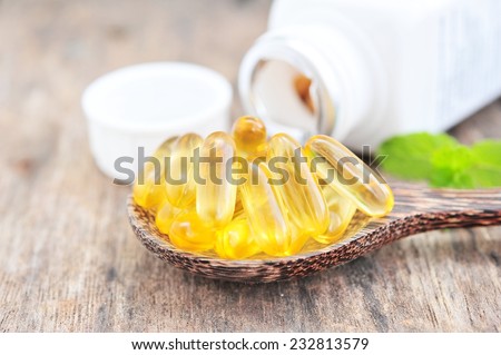 Cod liver oil omega 3 gel capsules on wooden spoon.