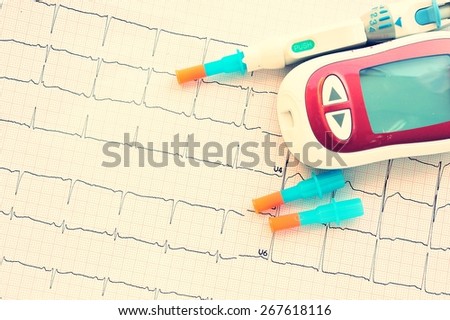 Blood sugar monitor with lancet pen on cardiogram chart.concept for measuring sugar level and health check.