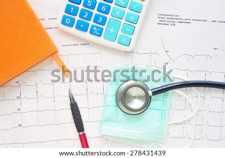 Stethoscope,pen,book and calculator on electrocardiogram paper.Health care costs.