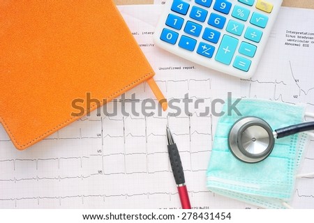 Stethoscope,pen,book and calculator on electrocardiogram paper.Health care costs.
