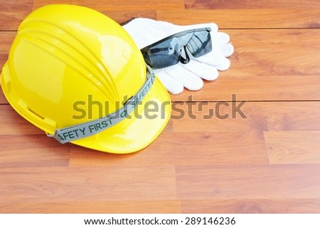 Yellow safety helmet ,glove and glasses on wooden floor.