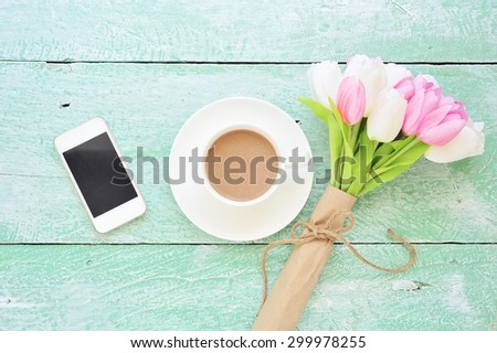White smartphone and coffee with bouquet of tulips on vintage wooden board.