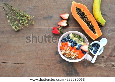 Bowl of fresh mixed  blackberries,banana,papaya,pumpkin seeds,chia pudding and yogurt on a wooden table.