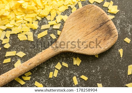 Grandmother\'s home made pasta and a kitchen spoon on black surface, yellow black background