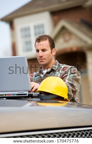 Construction: Home Builder Looks At Laptop.