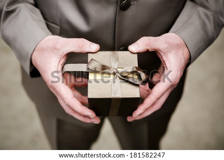 Groom in brown suit holding brown box (case) containing wedding rings