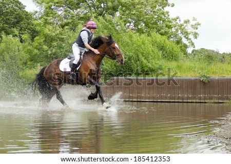 water jump-happy smiley rider and her horse enjoying riding through the water jump at an equestrian event on a summers day