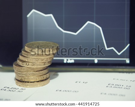 Pound coins on financial figures balance sheet with graph of decreasing exchange rate of the pound sterling. British Pound (GBP) currency after EU referendum result.