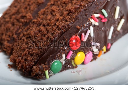 A slice of chocolate fudge cake, covered with dark chocolate icing and decorated with colorful sweets