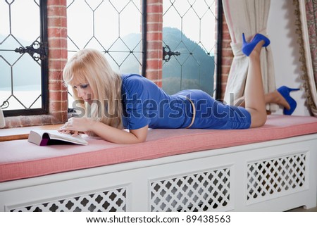 Blonde woman reading a book at the window