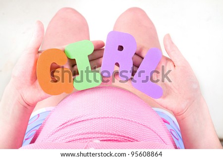 A pregnant woman is holding letter that spell out the word girl