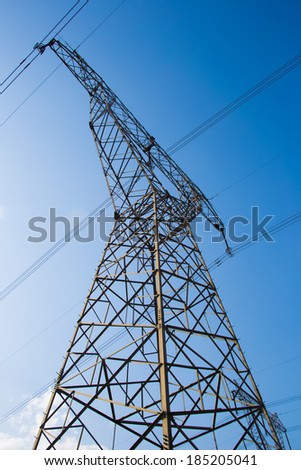 Electricity pylons and wires in a green field against blue sky.