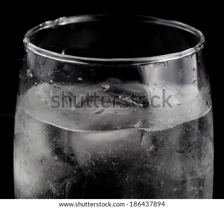 water with ice cubes in a glass cup on black background.