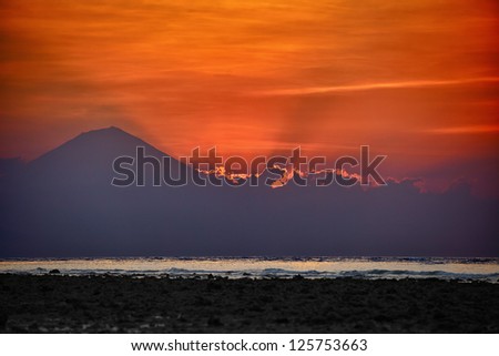Surrealistic sunset behind volcano and clouds with sea on front and red sky on background