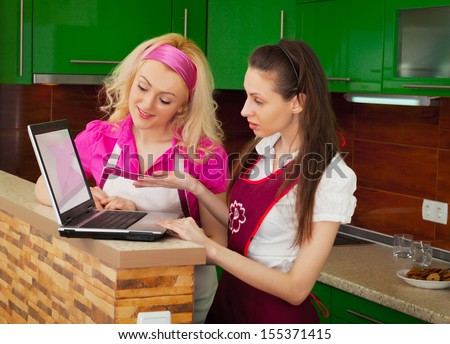 Two women with a laptop looking for a recipe in the Internet in the kitchen