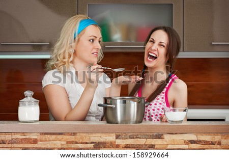 Two young girls try the soup in the kitchen