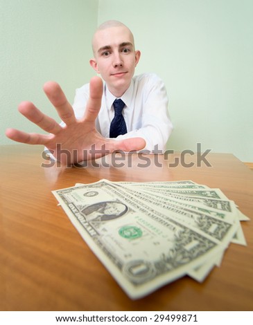 Young man reaches for a batch of money lying on a table