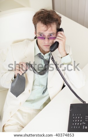 The young businessman speaks on the phone, worries and rumples a tie