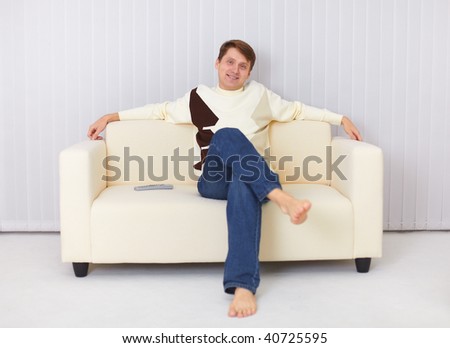 The happy guy sits on a sofa and watches TV