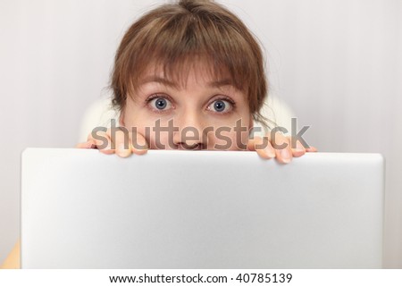 The amusing girl hides behind the laptop screen