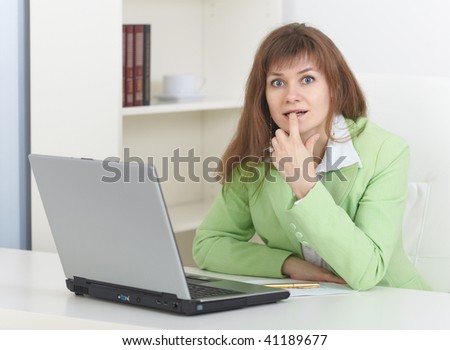 The young woman sits at a table at light office with the laptop