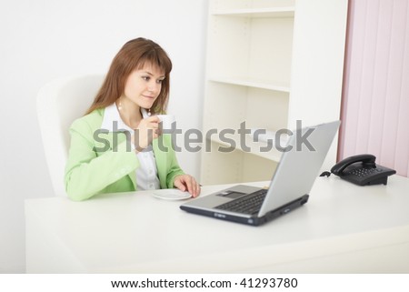 The young woman sits at a table at light office with the laptop