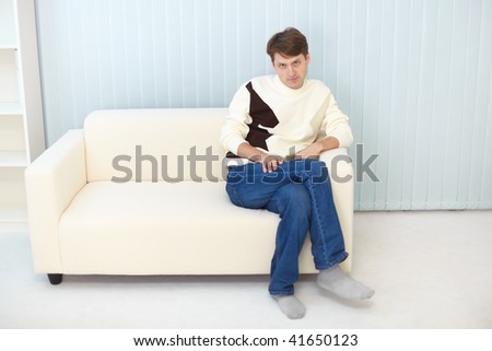 The person in jeans and sweater sits on a sofa