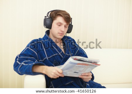 The man in the big ear-phones sits on a sofa reads the journal