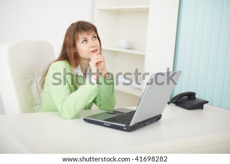 The dreamy woman sits at a table at light office with the laptop