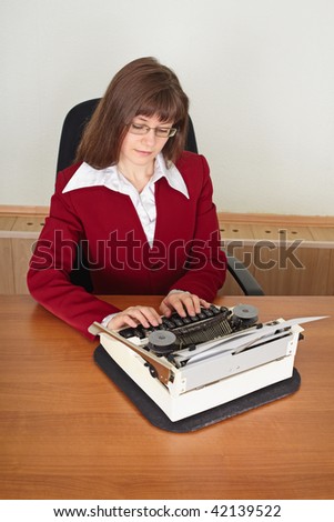 The woman prints on an ancient typewriter sitting at a table