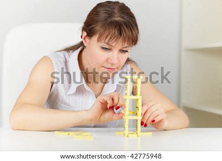 The young woman builds a tower on a table of dominoes