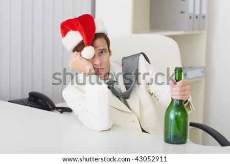 The young man in a christmas hat with a bottle sits at a table