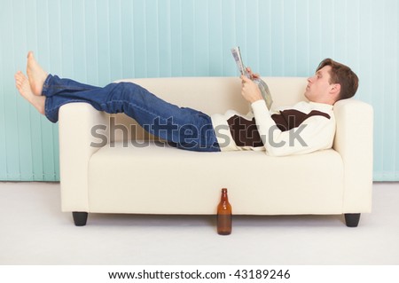 The person reads magazine comfortably lying on a sofa