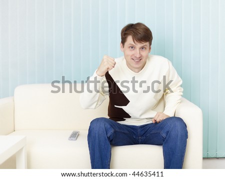 The guy sits on a sofa and watches football on TV