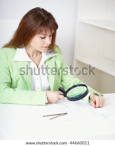 The beautiful girl works with the drawing by means of a magnifier