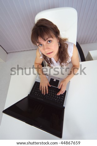 The amusing woman sits at a table with the computer - the top view