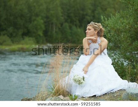 The sad bride sits on river bank and looks afar
