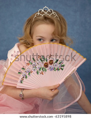 Beautiful girl hides behind her fan on blue