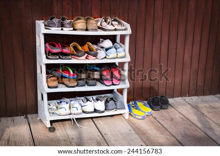 A variety of colorful shoes, neatly ordered on a plastic shoe rack outside a wooden house.