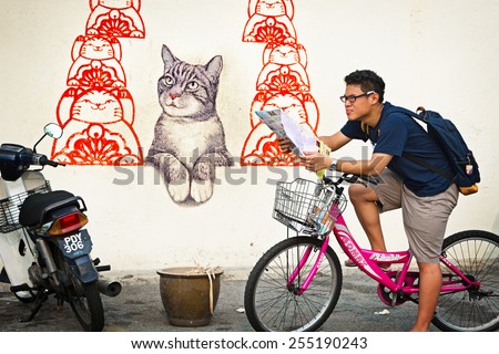 MALAYSIA, PENANG, GEORGETOWN - CIRCA JUL 2014: A tourist on a bicycle stops to examine his map in front of a mural of cats.