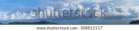 Beautiful panoramic shot of huge, billowing storm clouds, building and forming over the tropical sea near a popular tourist beach.